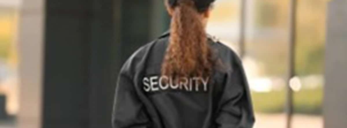 Una vigilante de seguridad de espaldas con un walkie talkie en la mano.