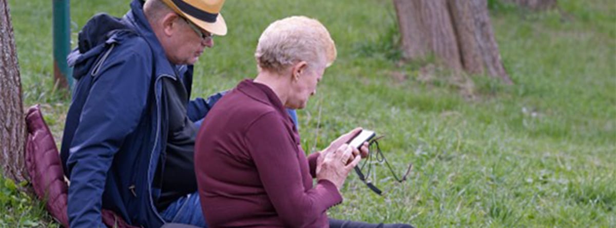 Matrimonio de personas mayores mirando el movil en un parque 