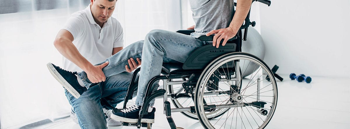 Fisioterapeuta ayudando a un hombre en silla de ruedas